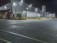 a factory with tanks at night time, in the background an industrial building with metal poles and overhead lighting