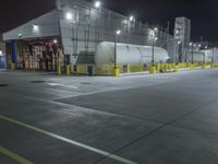 a factory with tanks at night time, in the background an industrial building with metal poles and overhead lighting