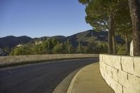 a concrete bridge next to the side of a road that is beside a hill with trees