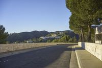 a concrete bridge next to the side of a road that is beside a hill with trees