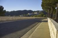 a concrete bridge next to the side of a road that is beside a hill with trees