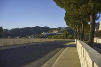 a concrete bridge next to the side of a road that is beside a hill with trees