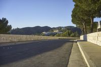 a concrete bridge next to the side of a road that is beside a hill with trees