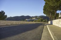 a concrete bridge next to the side of a road that is beside a hill with trees