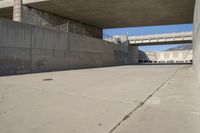 a road has concrete overpass and cement wall with cement under bridge area in background
