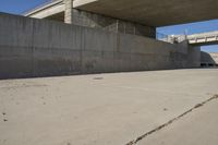 a road has concrete overpass and cement wall with cement under bridge area in background