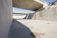 a road has concrete overpass and cement wall with cement under bridge area in background