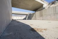 a road has concrete overpass and cement wall with cement under bridge area in background