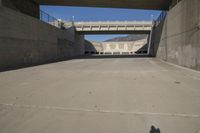 a road has concrete overpass and cement wall with cement under bridge area in background