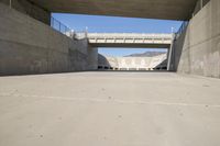 a road has concrete overpass and cement wall with cement under bridge area in background