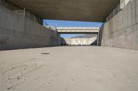 a road has concrete overpass and cement wall with cement under bridge area in background