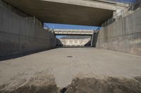 a road has concrete overpass and cement wall with cement under bridge area in background
