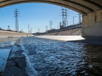 a view of water, electric poles, and street lights under an overpass over a body of water