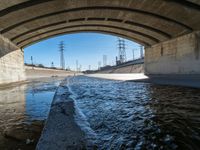 a view of water, electric poles, and street lights under an overpass over a body of water