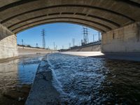 a view of water, electric poles, and street lights under an overpass over a body of water