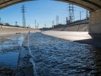 a view of water, electric poles, and street lights under an overpass over a body of water