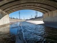 a view of water, electric poles, and street lights under an overpass over a body of water