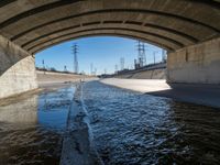 a view of water, electric poles, and street lights under an overpass over a body of water