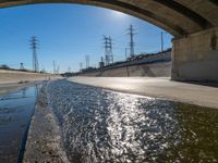 a view of water, electric poles, and street lights under an overpass over a body of water