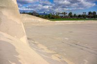 a skateboarder going down the side of an empty ramp and another person on the other side