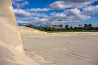 a skateboarder going down the side of an empty ramp and another person on the other side