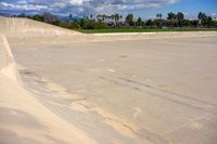 an empty concrete ramp with trees in the background and white clouds in the sky on the horizon