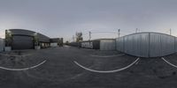 an empty parking lot with concrete walls and fencing in the middle of the photo is a large metal building