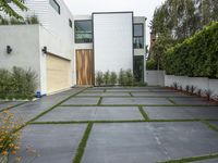 the driveway is full of concrete, grass and yellow flowers in the foreground of this contemporary residence