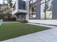 the contemporary residence has a green lawn and wooden stairs to the front door and large windows