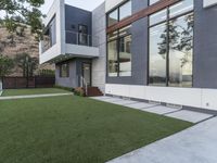 the contemporary residence has a green lawn and wooden stairs to the front door and large windows