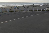 an empty road near a beach and waves as well as cars on the sand and houses on the beach