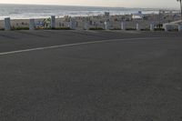 an empty road near a beach and waves as well as cars on the sand and houses on the beach