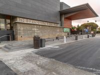 the entrance to an empty city bus station with benches next to the sidewalk and trash cans along one side