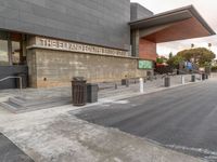 the entrance to an empty city bus station with benches next to the sidewalk and trash cans along one side