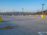 an empty parking lot is shown with yellow poles in the foreground and a large mountainside on the background