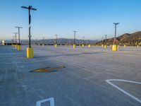 an empty parking lot is shown with yellow poles in the foreground and a large mountainside on the background