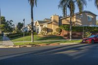 a red car is driving on the street near some houses and palm trees behind it