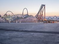 a large roller coaster is on the concrete surface by itself with an empty parking lot in front of it