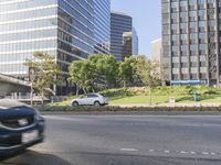 two cars driving down a street surrounded by high rise buildings and landscaping on either side