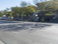 man riding his motorcycle down an empty street in motion with trees and houses behind him