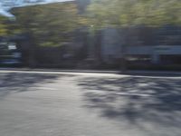 man riding his motorcycle down an empty street in motion with trees and houses behind him