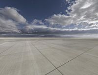 a plane sits on a tarmac under a cloudy sky, under which is a blue sky and mountains