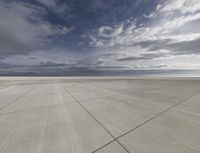 a plane sits on a tarmac under a cloudy sky, under which is a blue sky and mountains