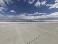 a plane sits on a tarmac under a cloudy sky, under which is a blue sky and mountains