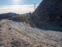 a dirt road in the desert with a mountain in the background that has power lines over it