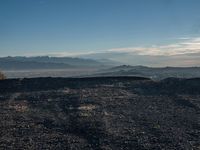 a person sitting on a mountain while looking at the horizon to see a fire burning