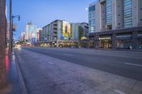 a city street at dusk with buildings and shops lining both sides of the road and a pedestrian on the sidewalk