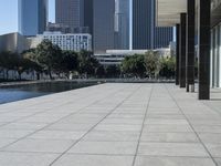 a paved concrete sidewalk surrounded by tall buildings and a pond at the end of it