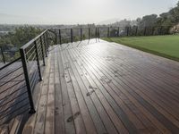 a wooden deck with grass and a fenced in view of a golf course with hills and trees