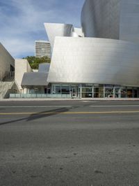 an empty street in front of a large white building with glass walls on the sides